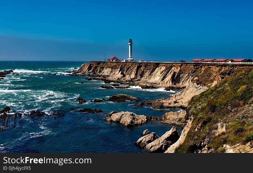 White Lighthouse Near Body of Water Under Blue Sky during Daytime