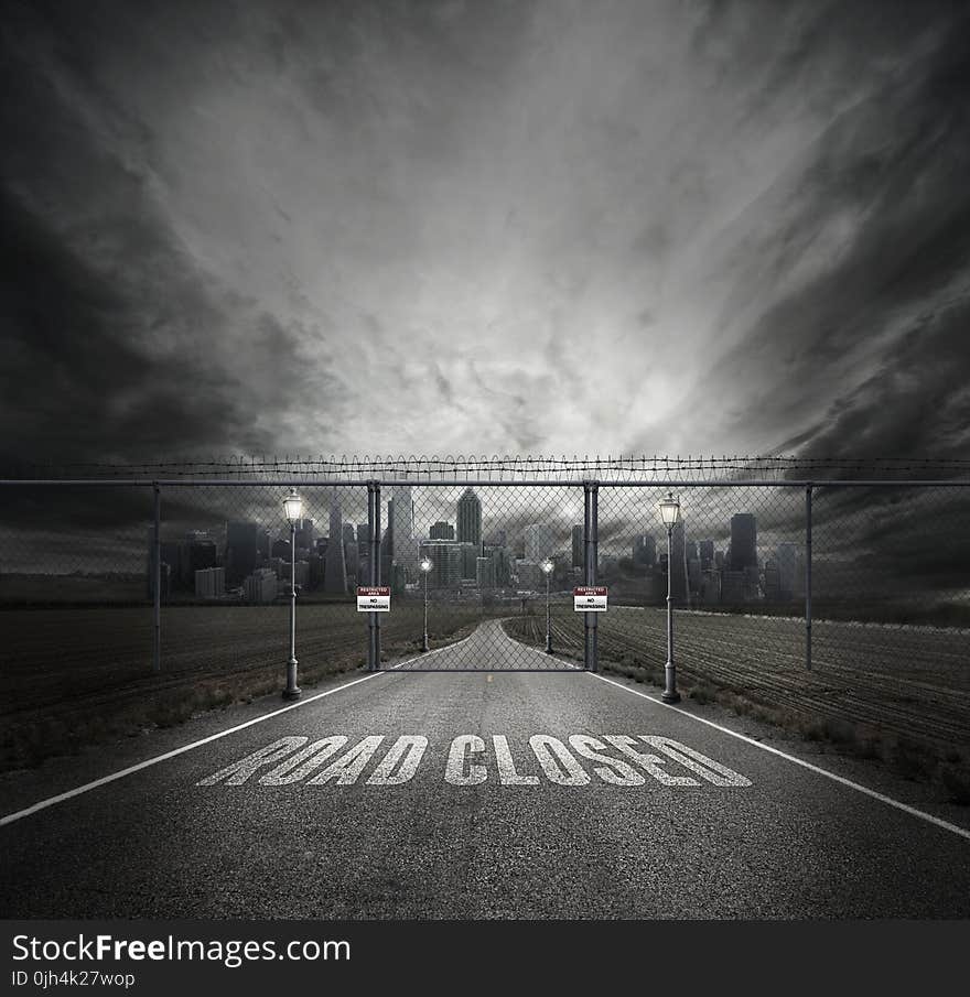 Grayscale Photo of Road Closed on Roadway With Gray Fence Gate in Front of City