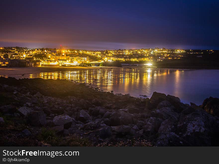 Lighted City in Distance Near Body of Water