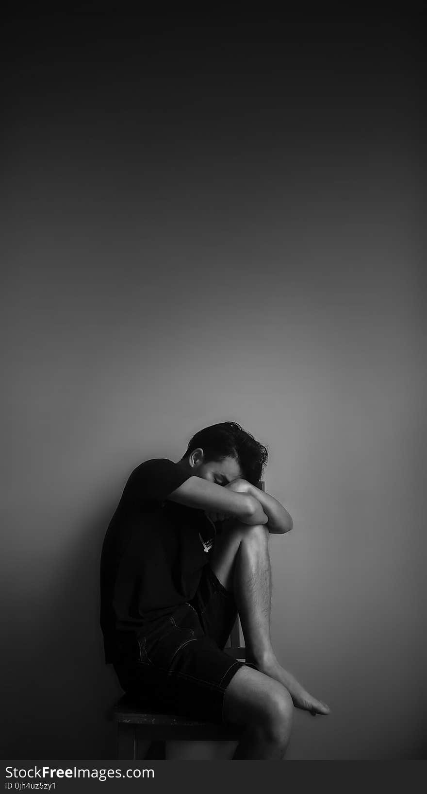 Grayscale Photography of Man Sitting Beside Wall