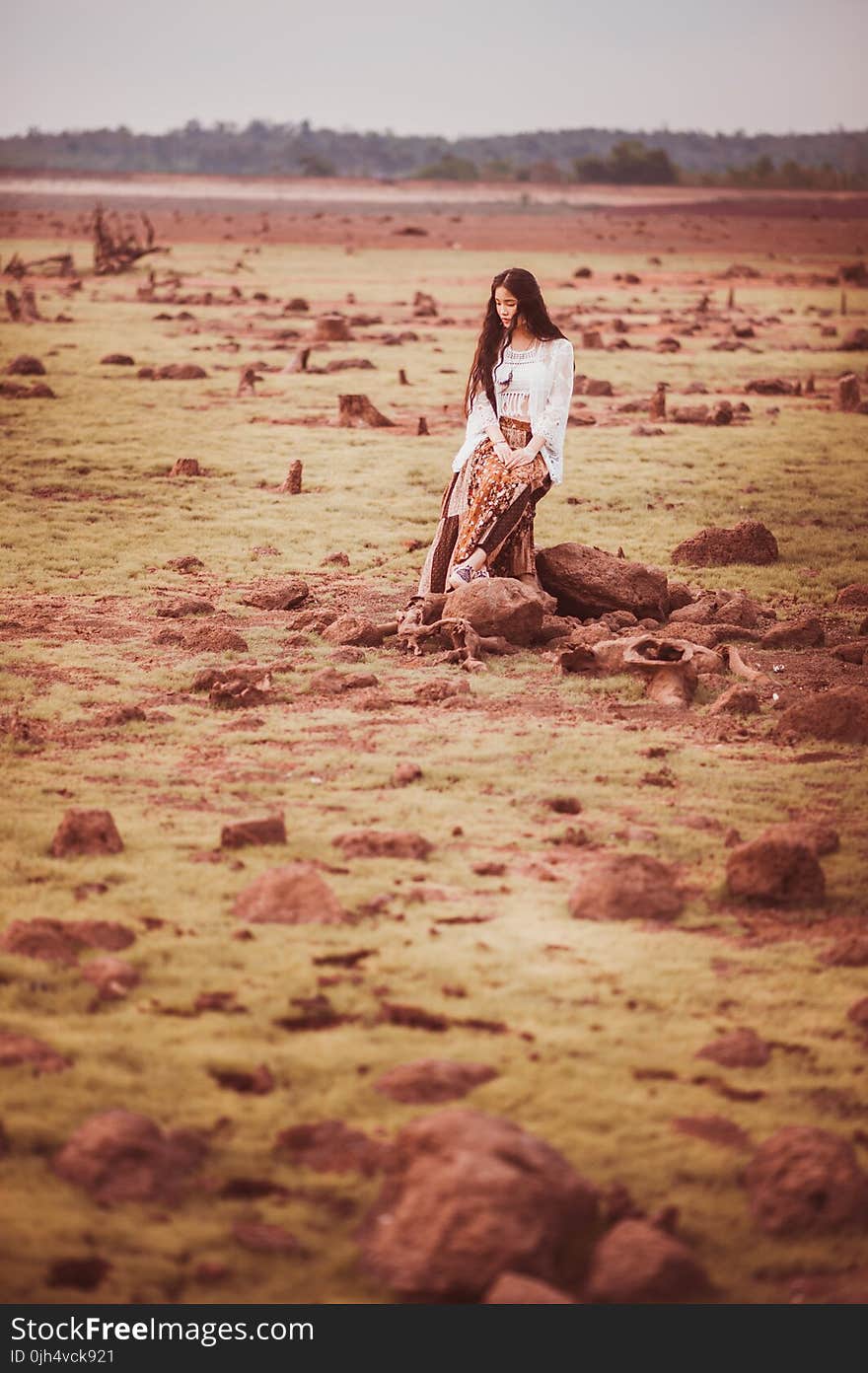 Woman in White Cardigan and Brown Pants Sitting on Stump during Daytime