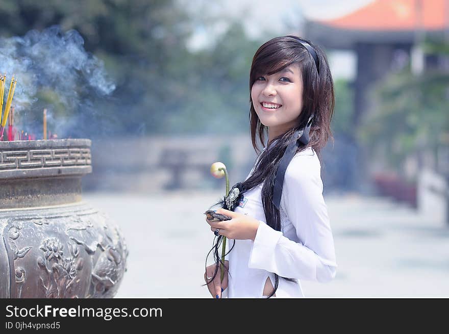 Smiling Woman in White Long Sleeved Top Holding Beige Petaled Flower Posing for Photo during Daytime