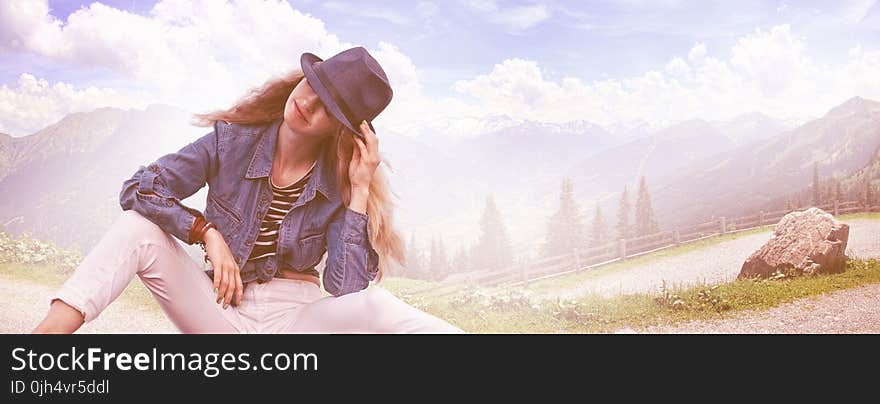 Woman Wearing Black Fedora Hat, Blue Denim Blazer and White Skinny Jeans While Sitting on Ground