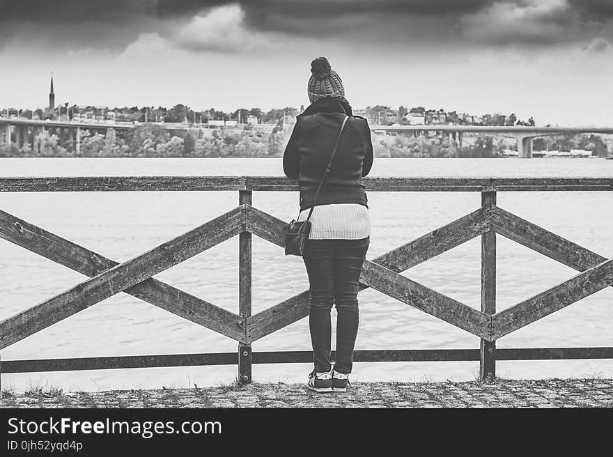 Woman Near Wooden Railing and Body of Water Grayscale Photo