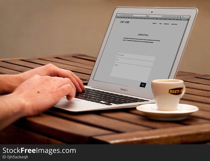 Human Using Laptop Beside Teacup on the Wooden Table