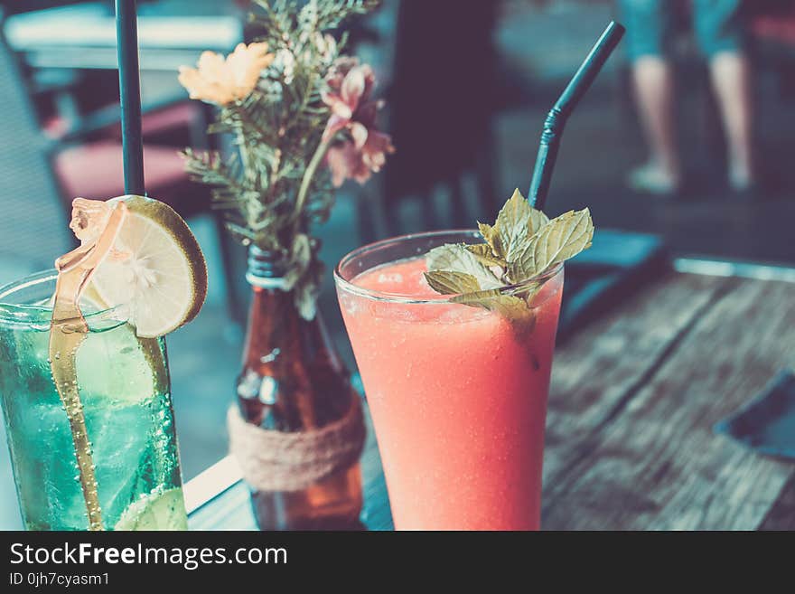 Glass of Fruit Juice Next to a Bottle With Flowers and Clear Glass Cup