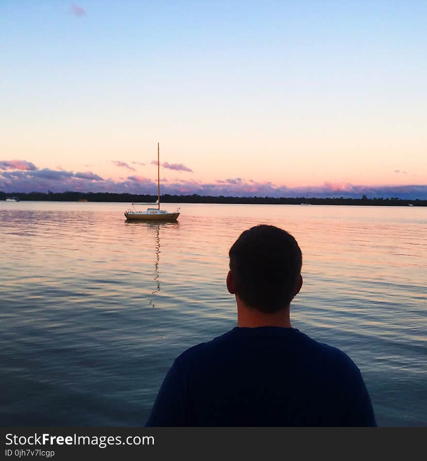 Man in Blue Shirt Near Blue Sea and White Boat Under Blue Sky