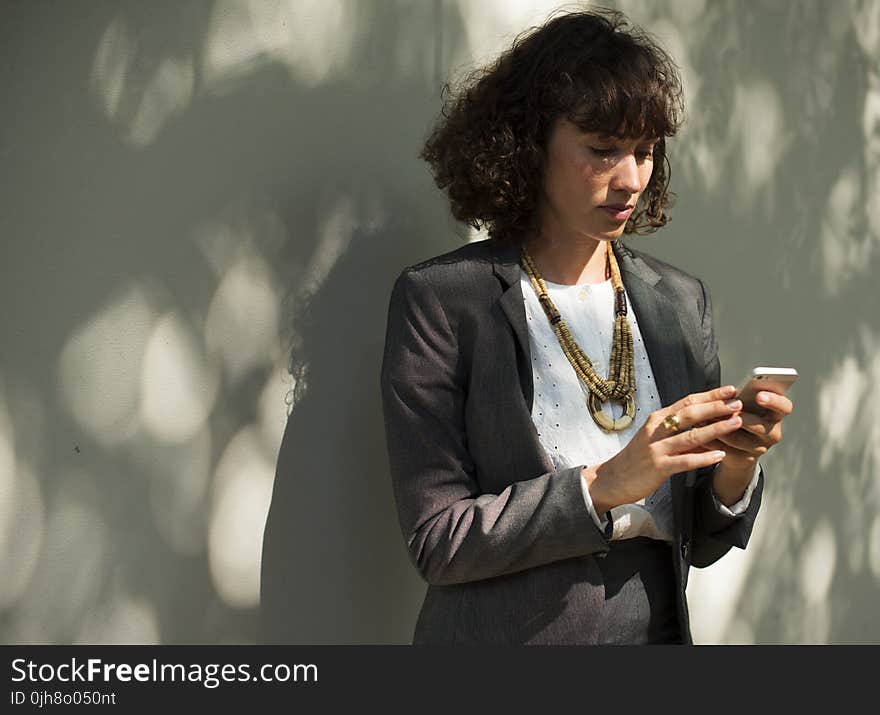 Woman In Black Blazer Holding A Smartphone While Standing Near Wall