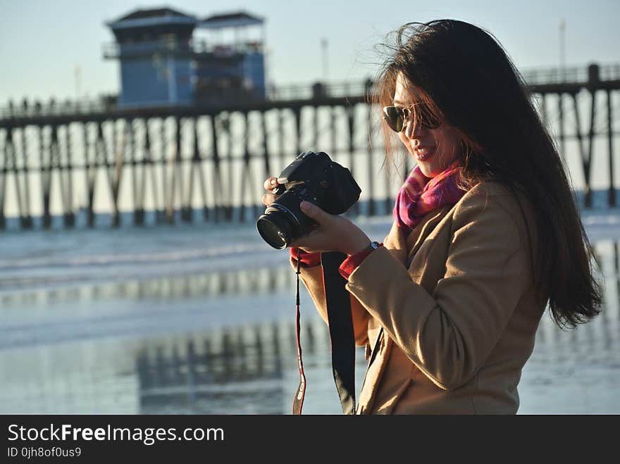 Selective Focus Photography of Woman Holding Her Camera Near Seashore