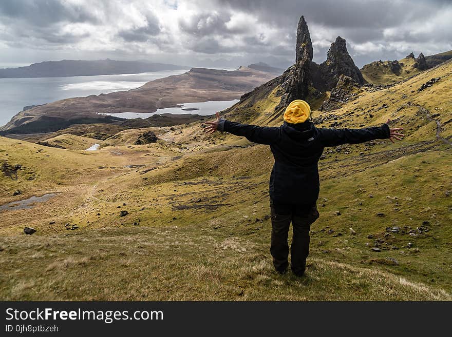 Person Wearing Black Jacket Standing on Green Grass Field Near Lake