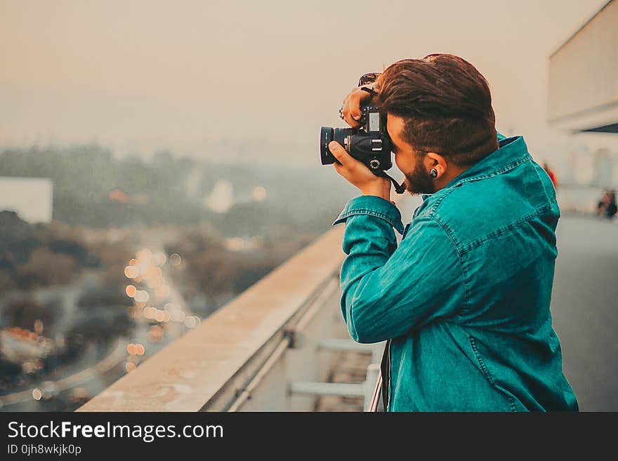 Man In Teal Button-Up Long Sleeved Shirt Shooting Using DSLR Camera