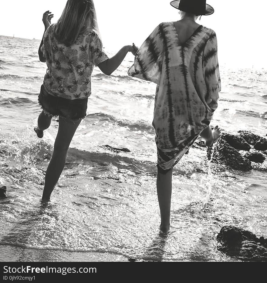 Grayscale Photograph of 2 Women Holding Hands While Walking on Sea Shore