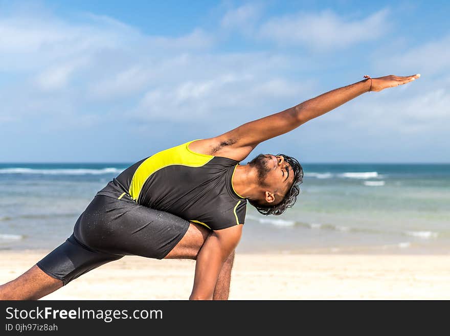 Man in Yellow and Black Tank Top Doing Exercise on Seashore at Daytime