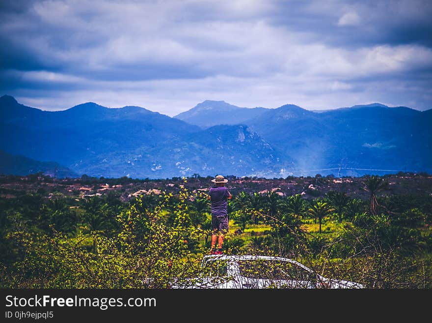 Person Wearing Sun Hat Looking At Mountains Under Cloudy Sky