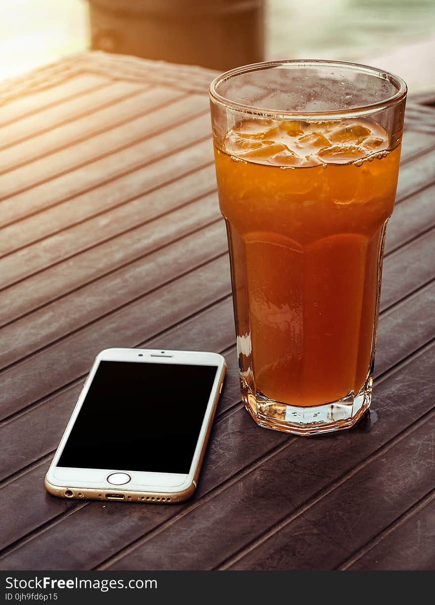 Orange Juice in Clear Drinking Glass Besides Gold Iphone 6 on Brown Wooden Table