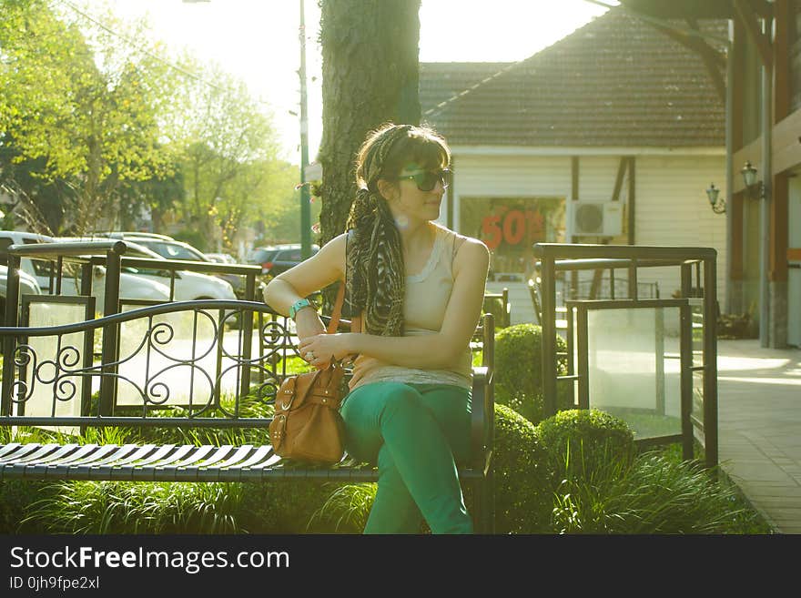 Woman in Brown Tank Top Sitting on Black Bench Beside Tree