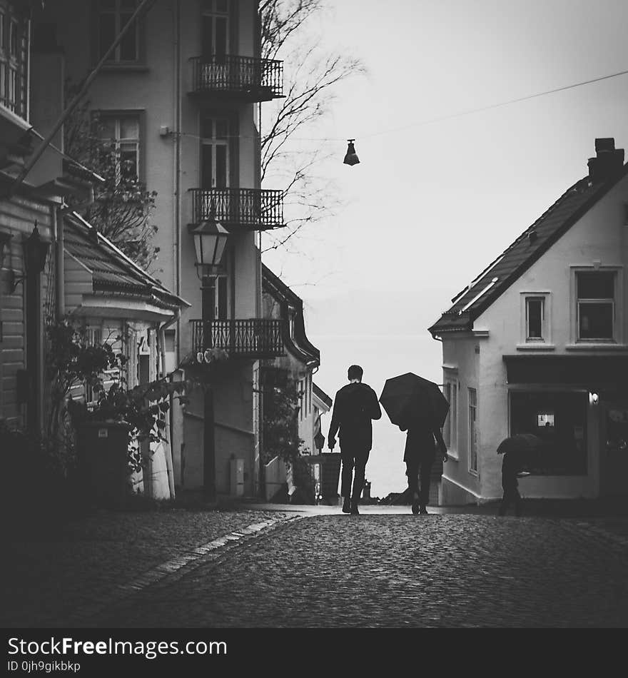 Grayscale Photo Of Man Beside Woman Under Umbrella Walking On Pavement