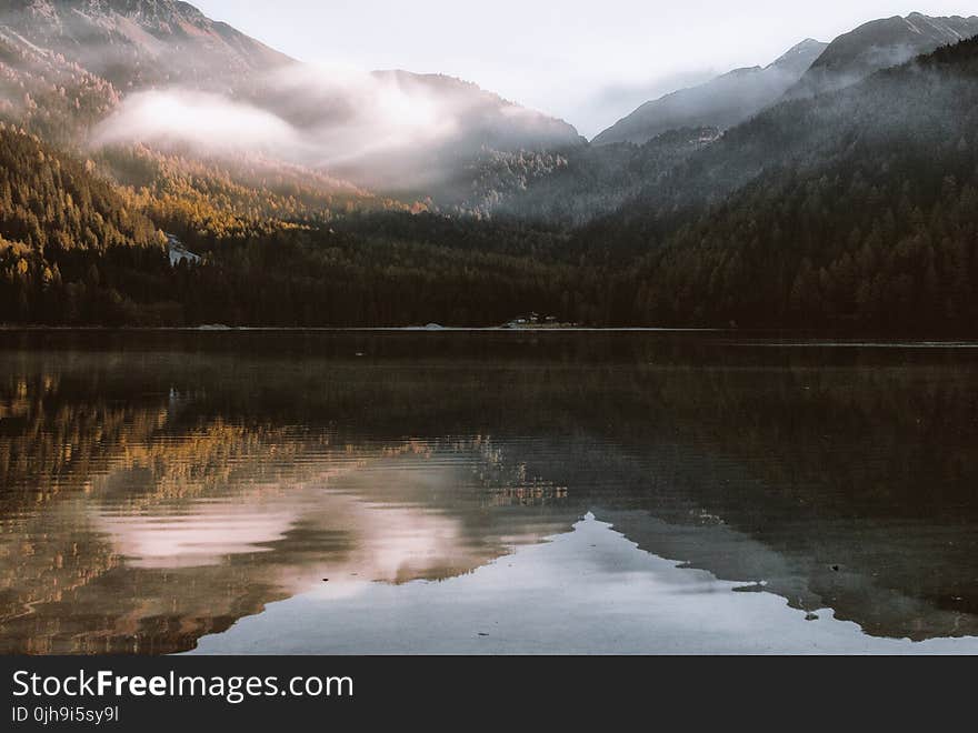 Mountain Reflection on Body of Water Under White Sky at