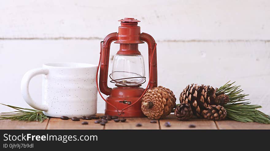 Red Kerosene Lantern Beside White Ceramic Mug on Brown Wooden Table