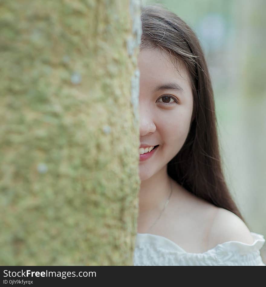 Woman in White Off-shoulder Top Behind Grey Tree Trunk