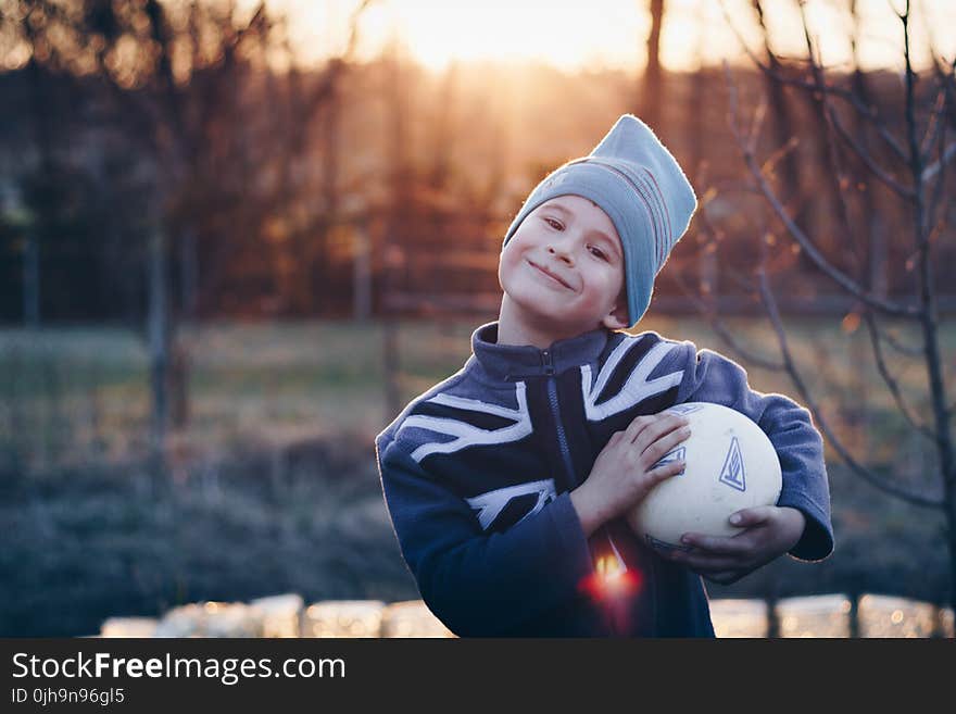 Selective Focus Photography of Boy Wearing Blue United Kingdom Print Zip-up Jacket Carrying White Ball