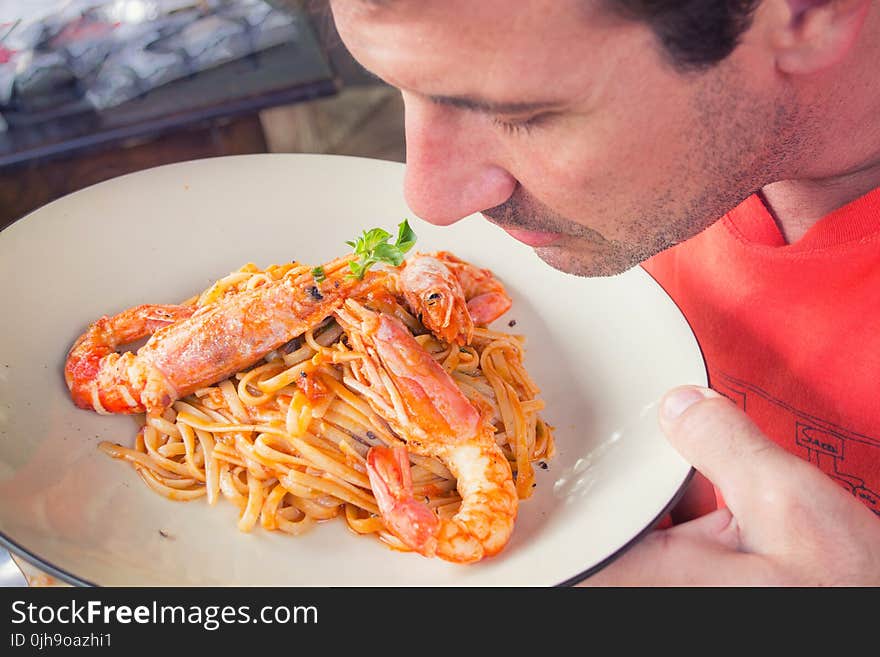 Man Smelling Prawn and Pasta Dish on White Ceramic Plate