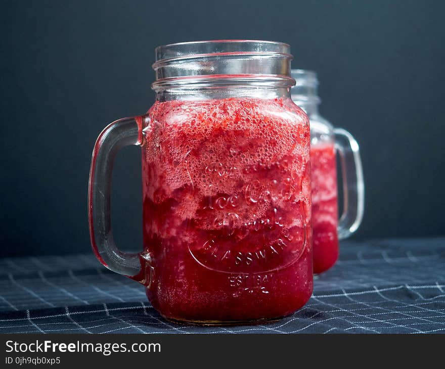 Closeup Photography of Two Clear Glass Jar Filled With Red Liquid on Top of Blue and White Tattersal Textile