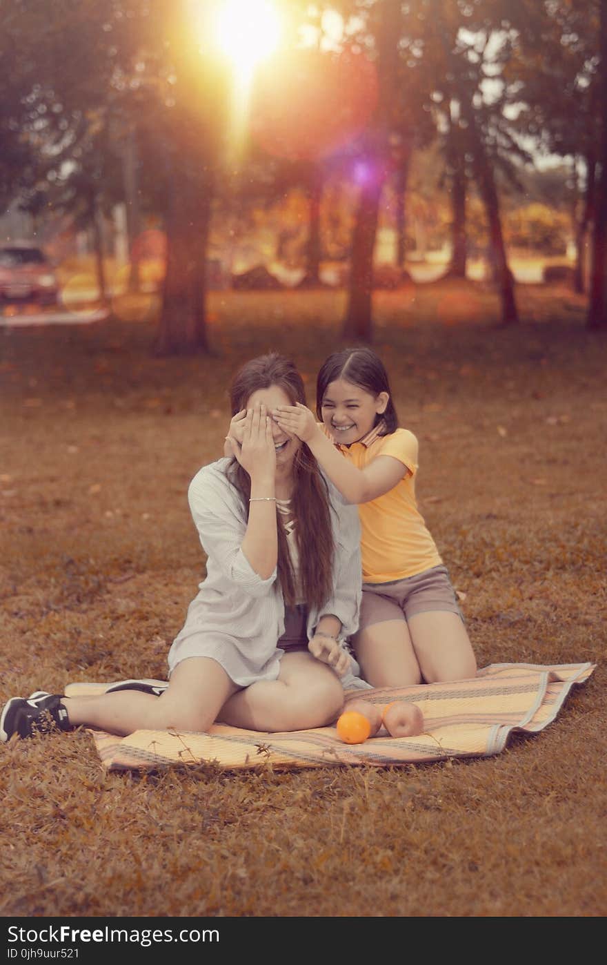 Two Women Sitting on Brown Picnic Mat during Sunset