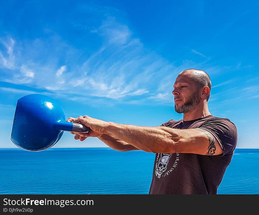 Man Wearing Black Shirt Holding Kettle Bell Near Body of Water