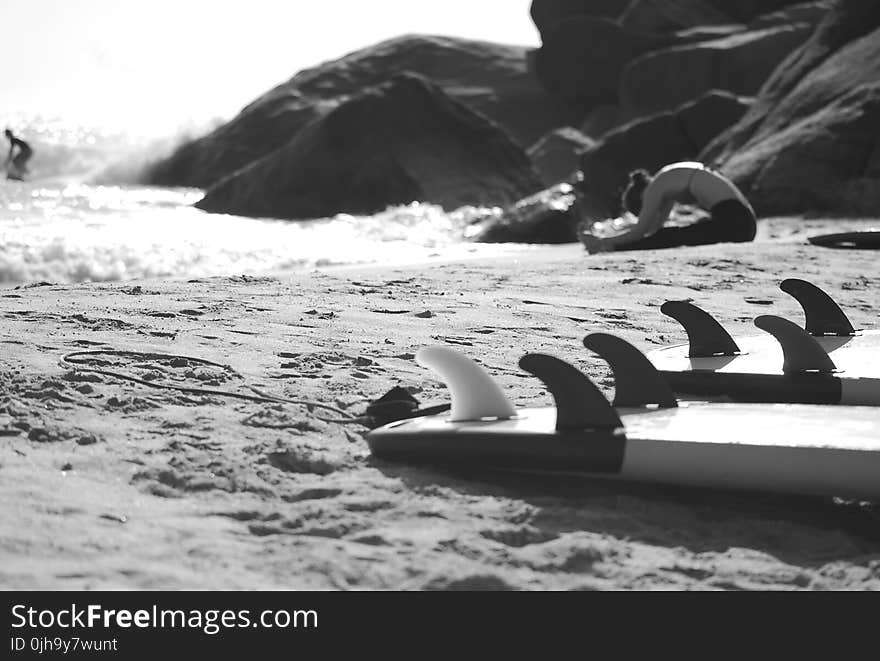 Grayscale Photo of Woman Sitting on Beach Near Rock Formation