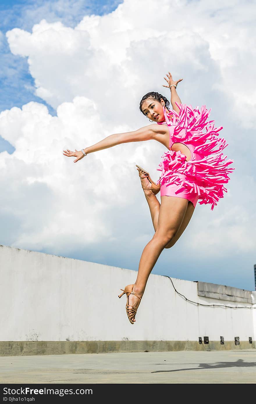 Woman in Pink Dress Doing Jump Shot While Extending Arms Under White Clouds