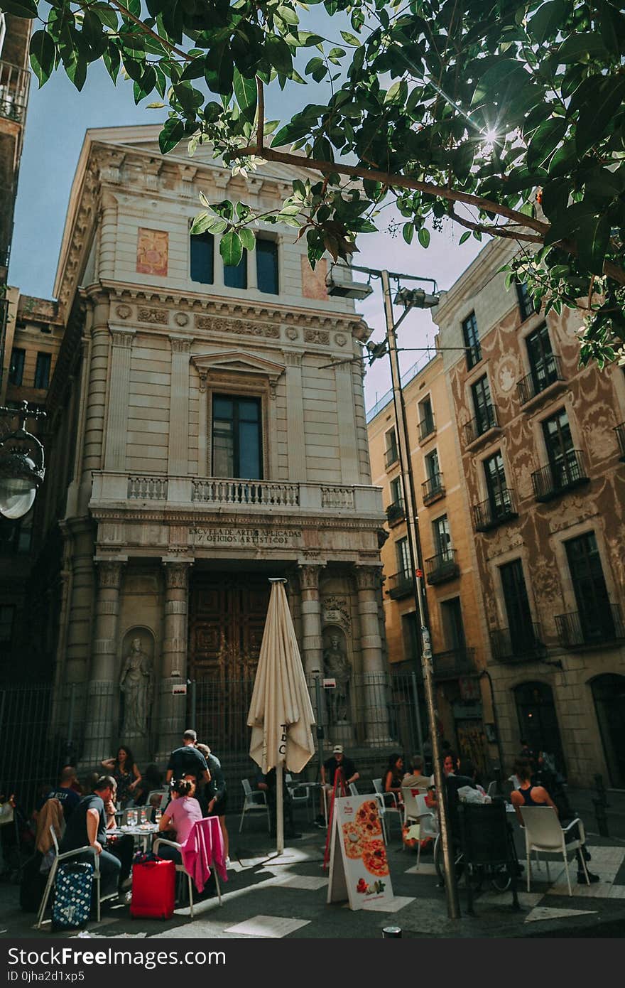 Brown Concrete Building With People Sitting on Patio Sets Photo Taken