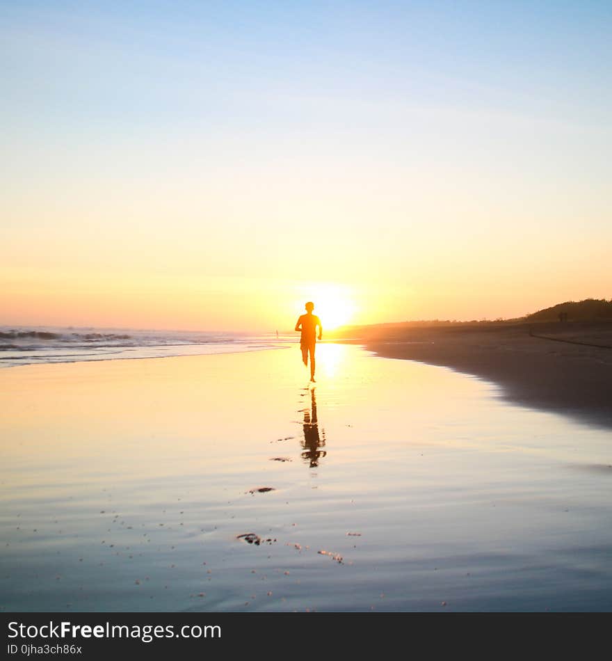 Silhouette of Boy Running in Body of Water during Sunset