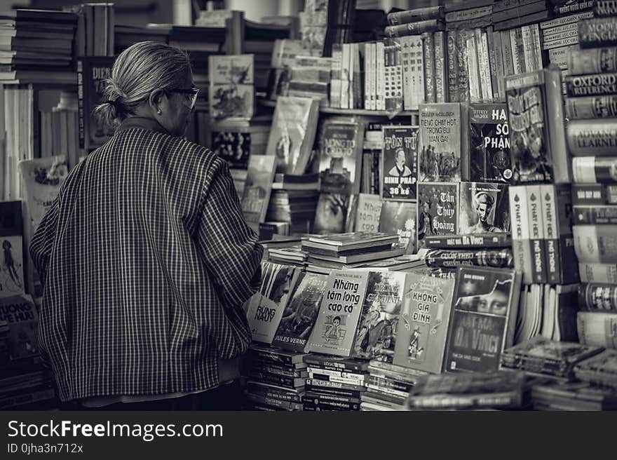 Person Standing in Front of Assorted Books in Gray Scale Photography