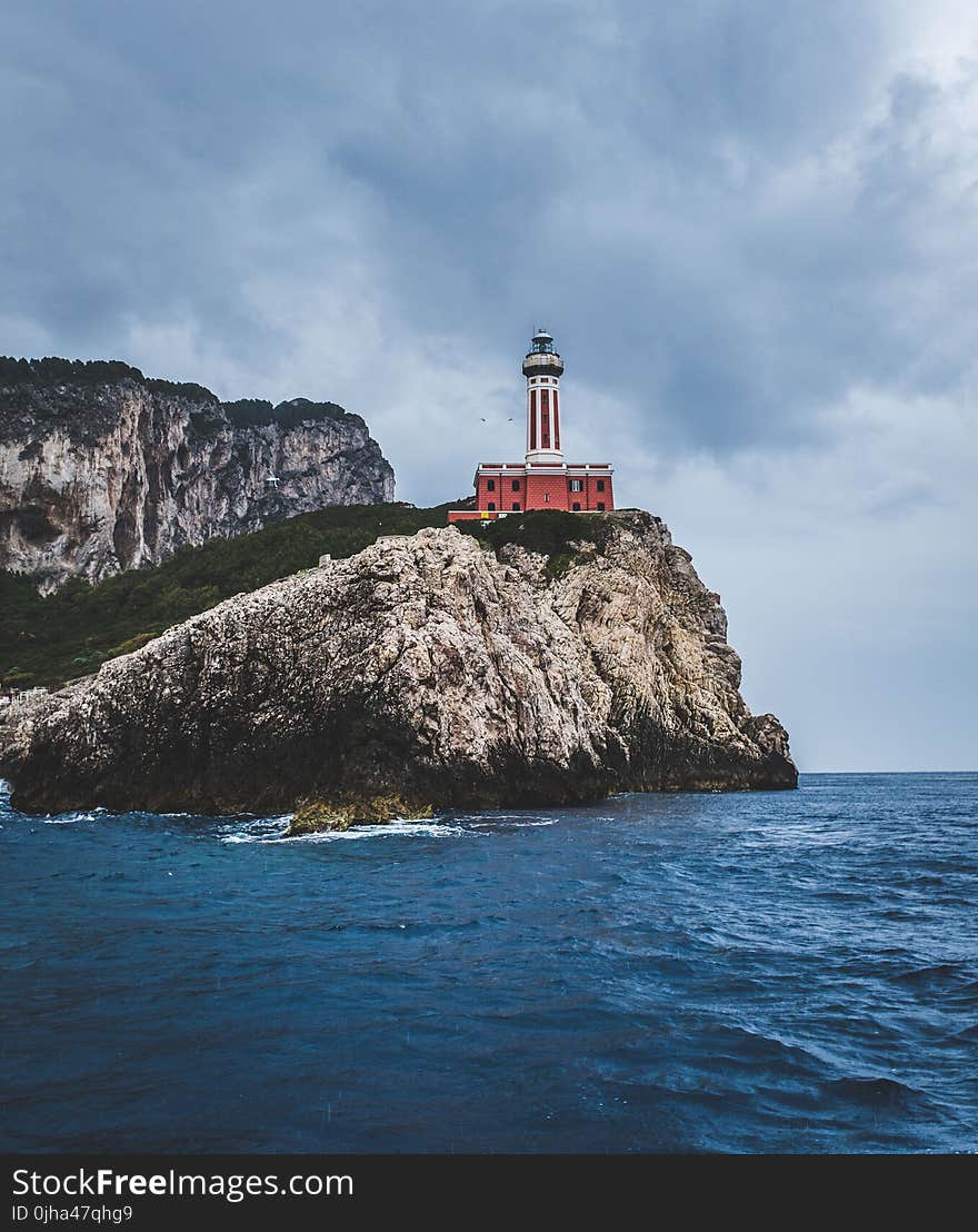 Red Lighthouse on Top of Hills Beside Sea