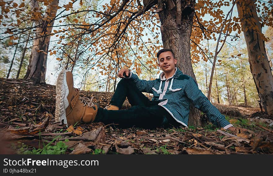 Man Wearing Green Jacket Sitting on Ground Near Tree