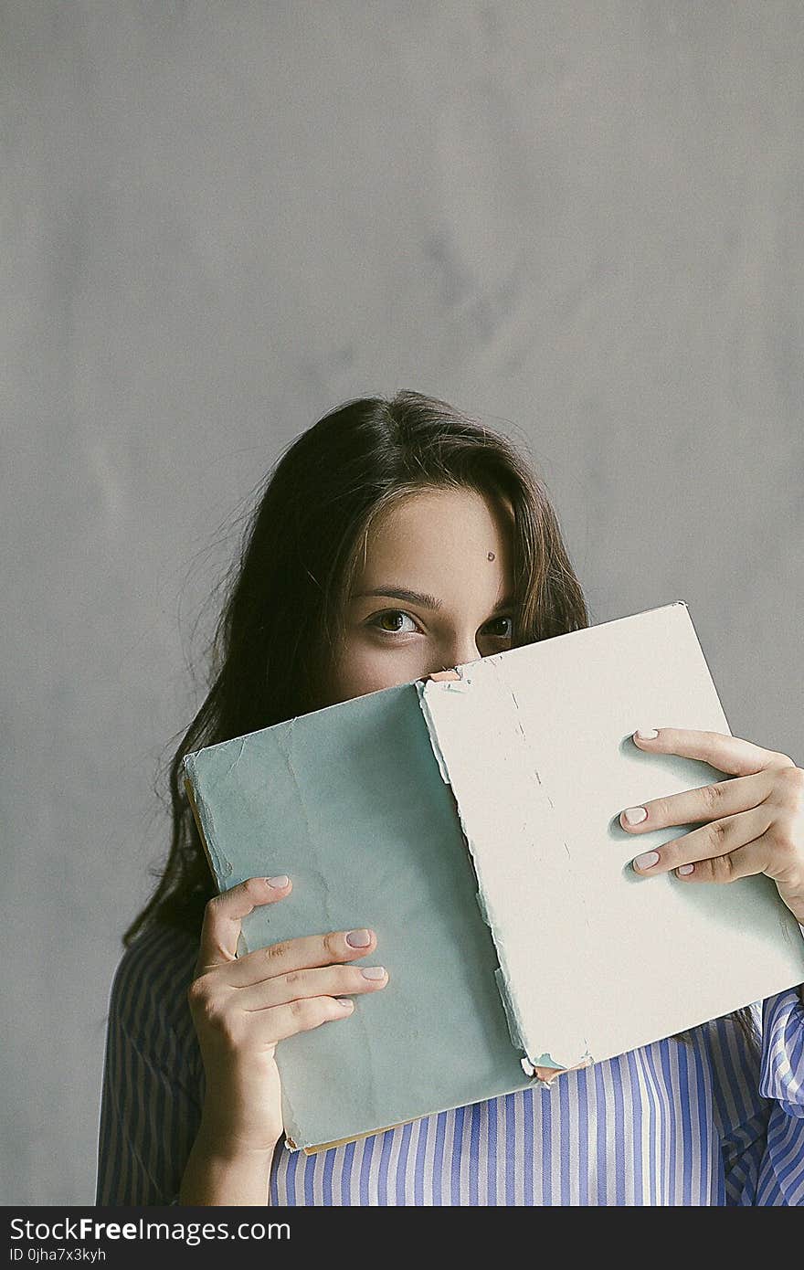 Woman in Blue Striped Flannel Shirt Holding a Book Indoors