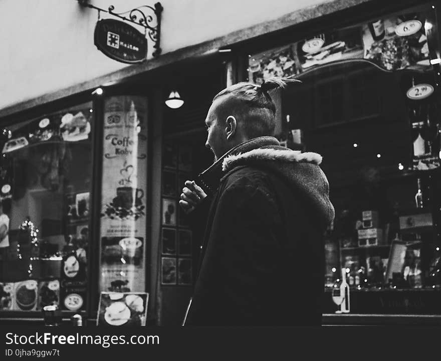 Grayscale Photograph of Man Walking Past by Shop