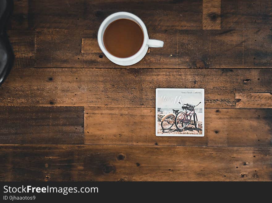 White Ceramic Mug With Coffee Beside Photo of Two Mountain Bikes