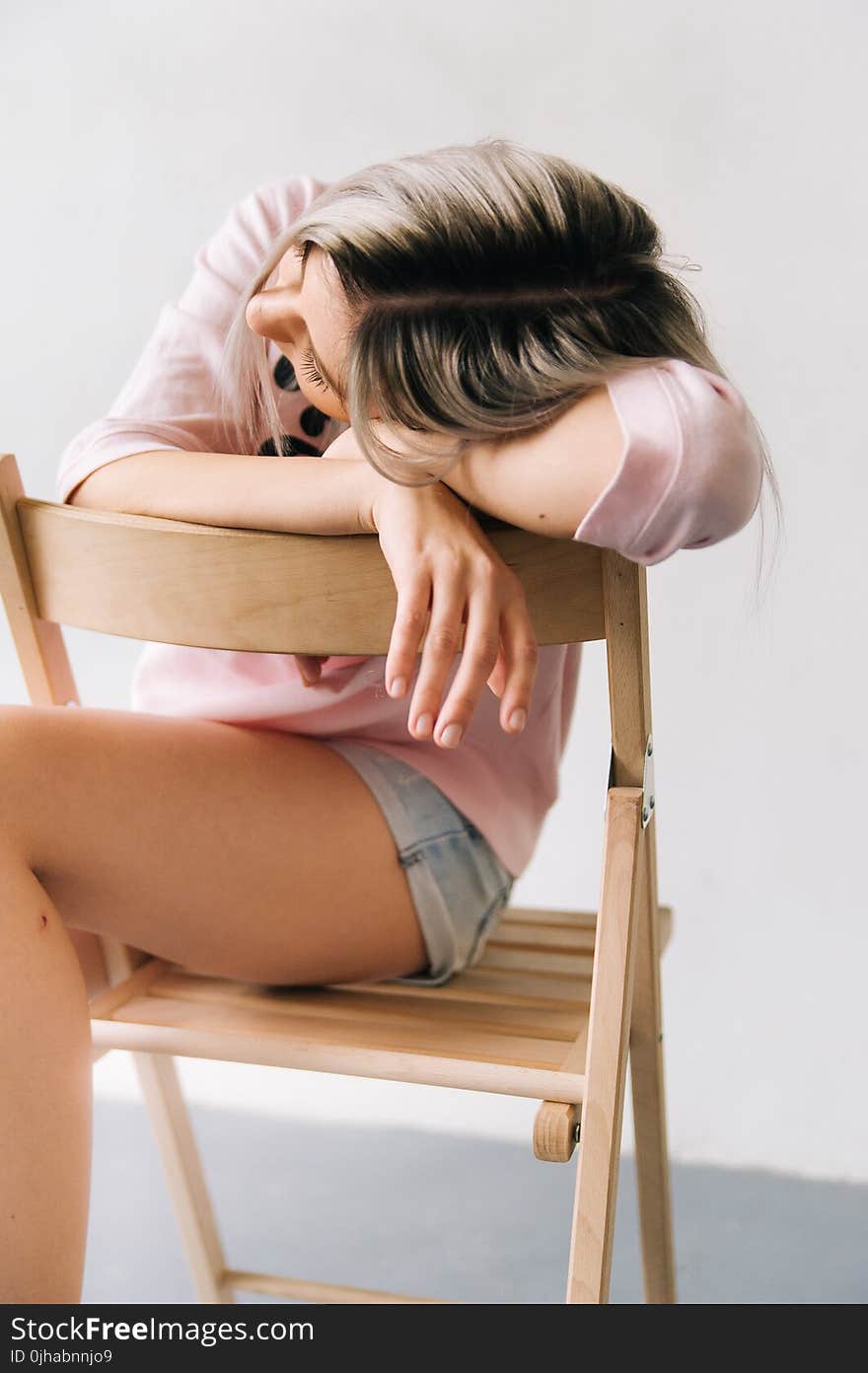 Woman Wearing Pink Long Sleeve Shirt and Blue Denim Short Shorts Sitting on Brown Wooden Folding Chair