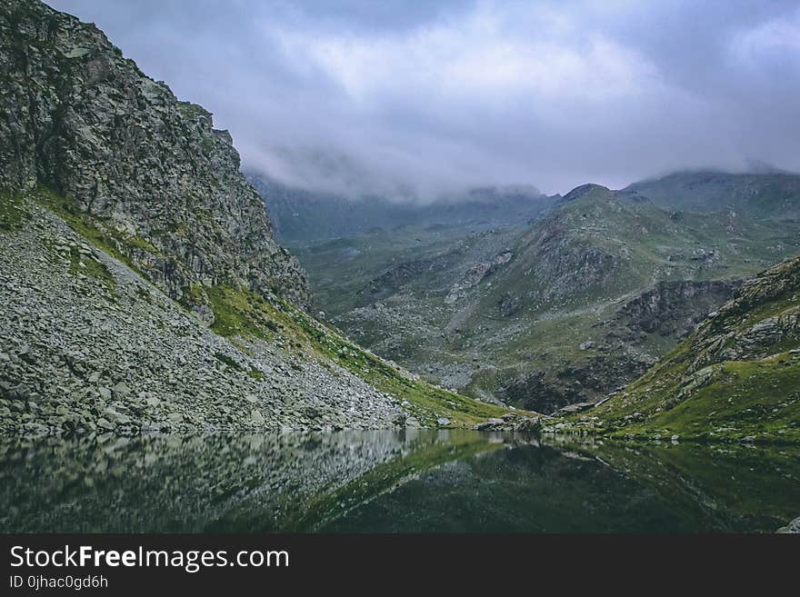 Gray and Green Mountains With Body of Water Under Cloudy Sky