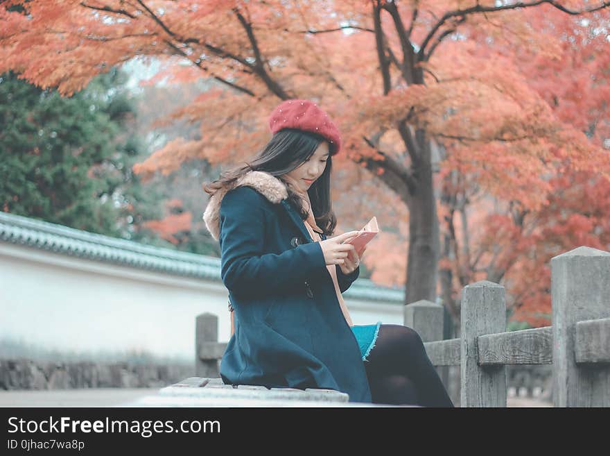 Woman in Blue Parka Jacket Sitting on Grey Concrete Bench Reading Book