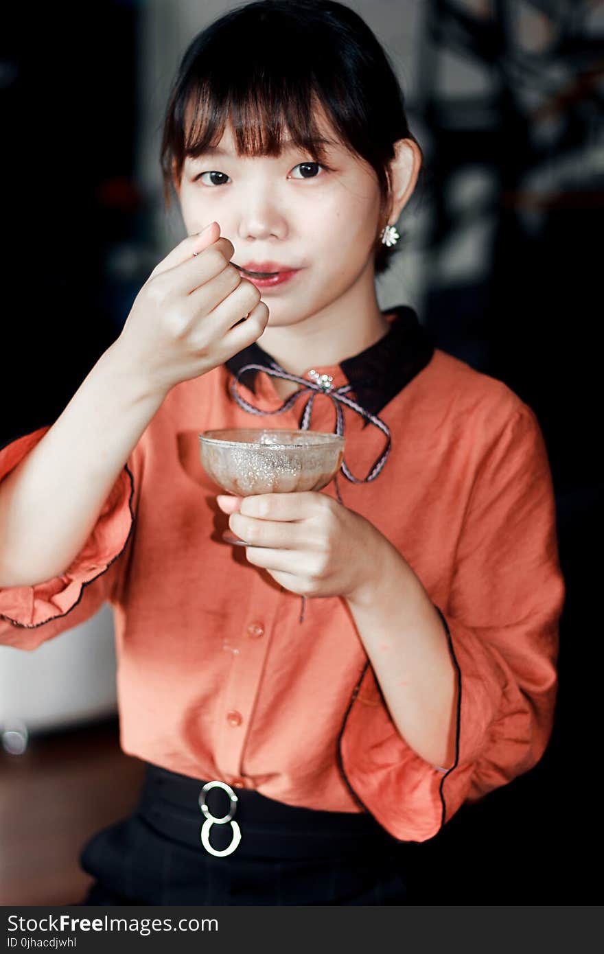 Woman in Orange Dress Holding Brown Liquid Filled Glass Cup