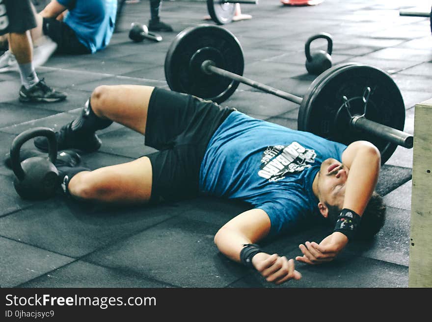 Man Lying on Rubber Mat Near Barbell Inside the Gym