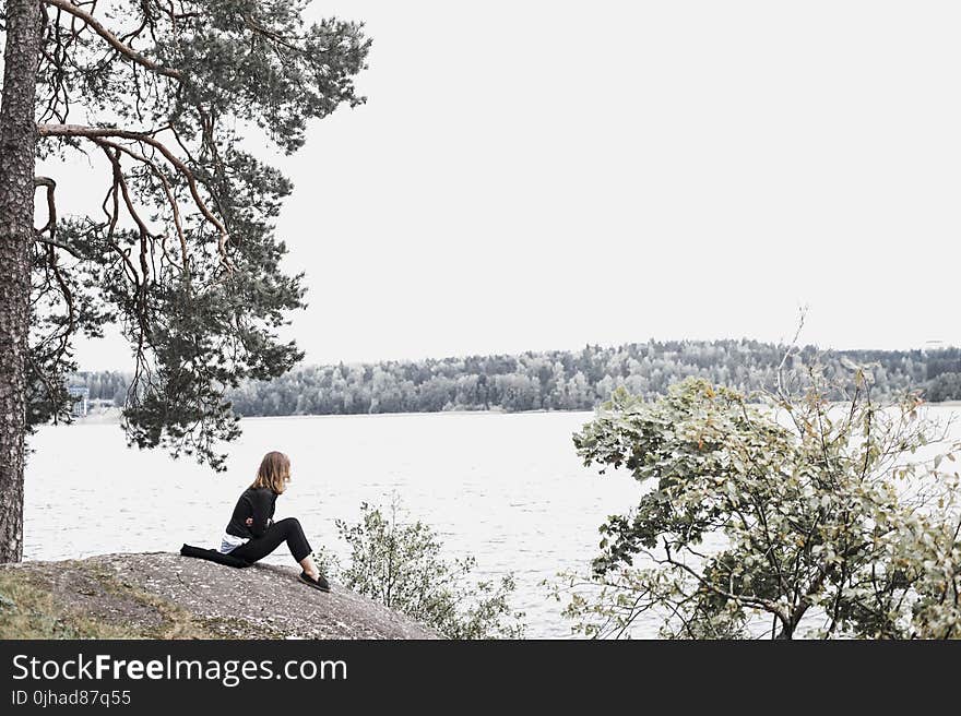 Woman Sitting on Gray Soil Near Body of Water