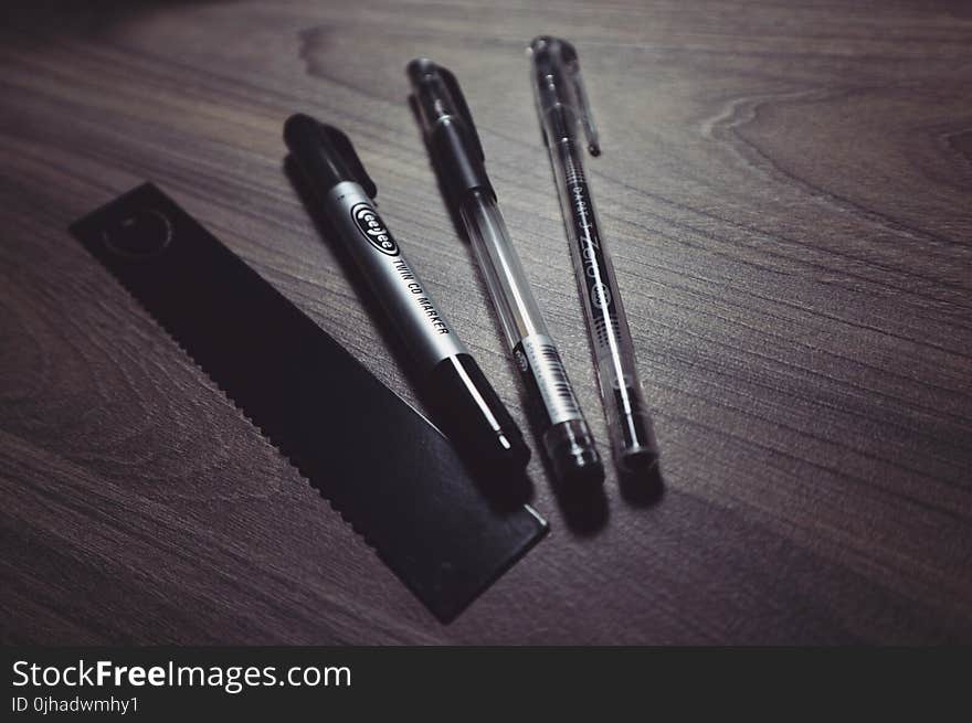 Three Ballpoint Pens and Black Ruler on Beige Wooden Surface