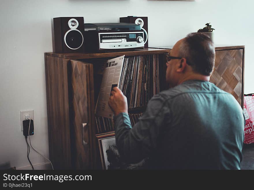 Man in Gray Longsleeve Shirt Holding Book in Front of Brown Wooden Book Case