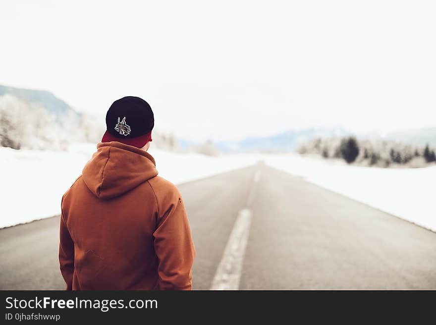 Person in Brown Hoodie Standing on Asphalt Road