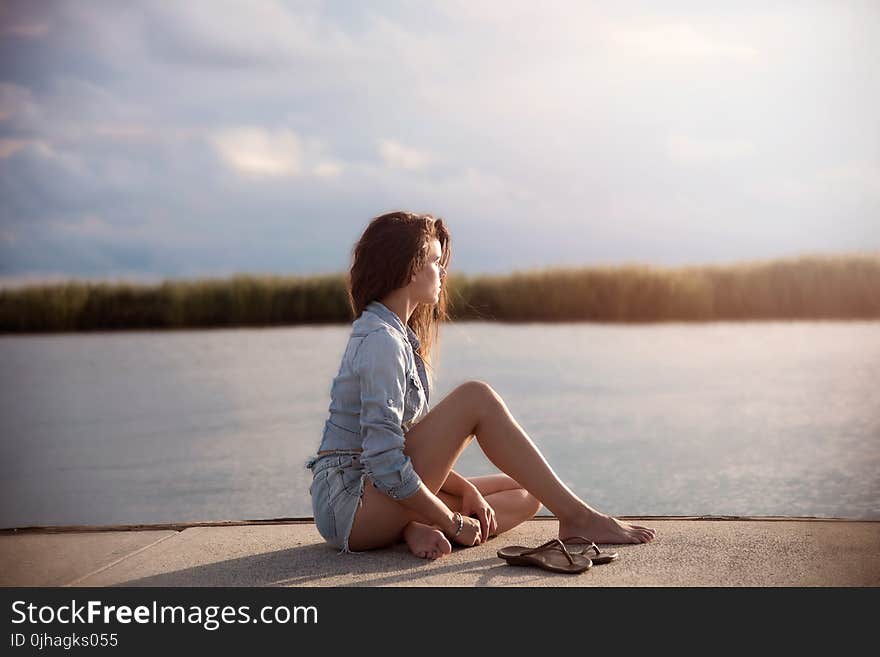 Woman In Blue Denim Jacket Sitting Near Body Of Water