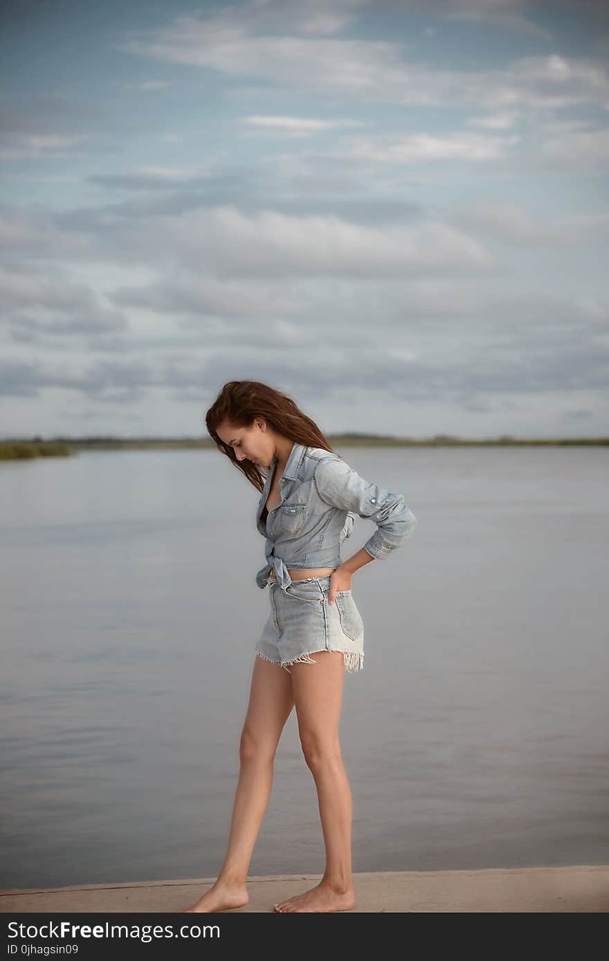 Woman Wearing Gray Denim Tie-front Long-sleeved Shirt and Short Shorts Walking on Isle Near Body of Water